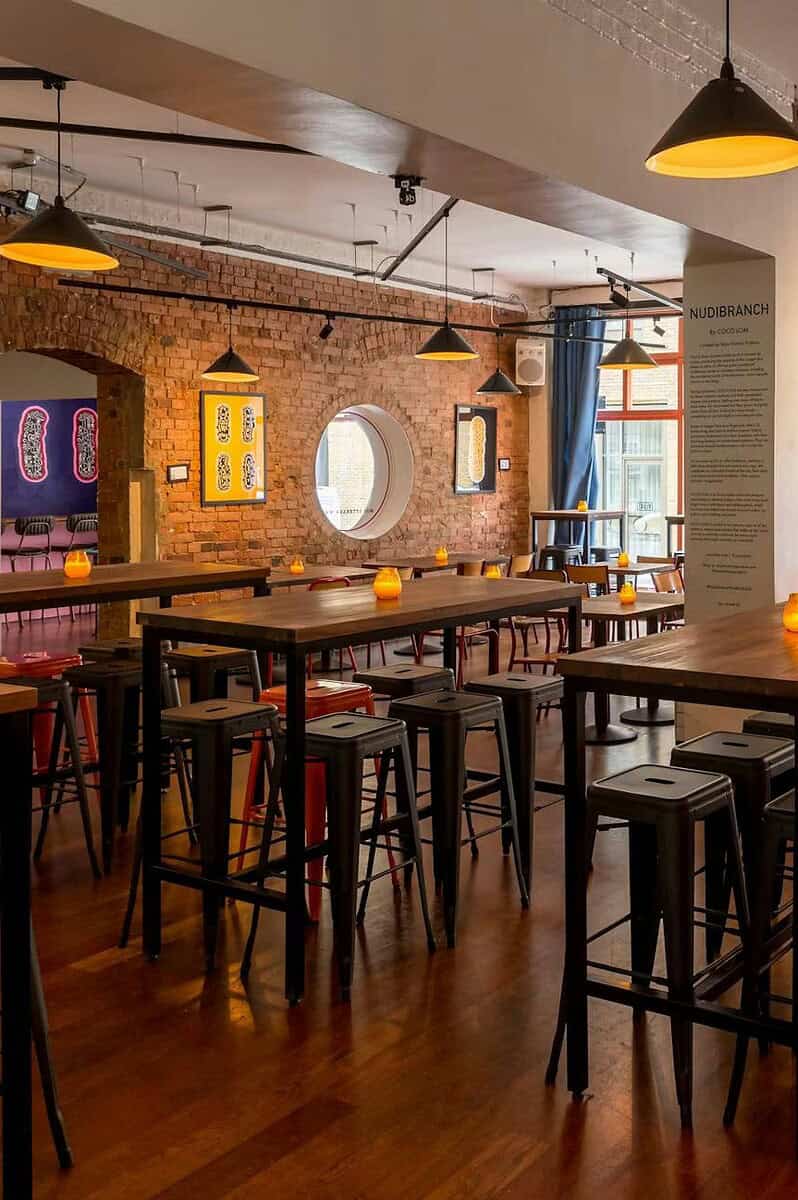 A vibrant, modern cafe interior with exposed brick walls, large windows, and stylish seating arrangements, perfect for socializing or working in a cozy, inviting atmosphere.