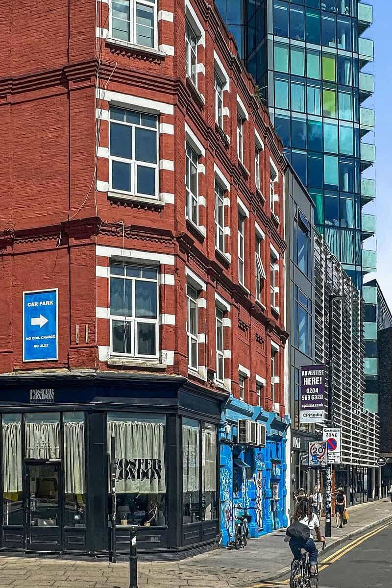 A vibrant city street scene featuring a historic red brick building with modern glass structures in the background, showcasing urban architecture and bustling city life in London.