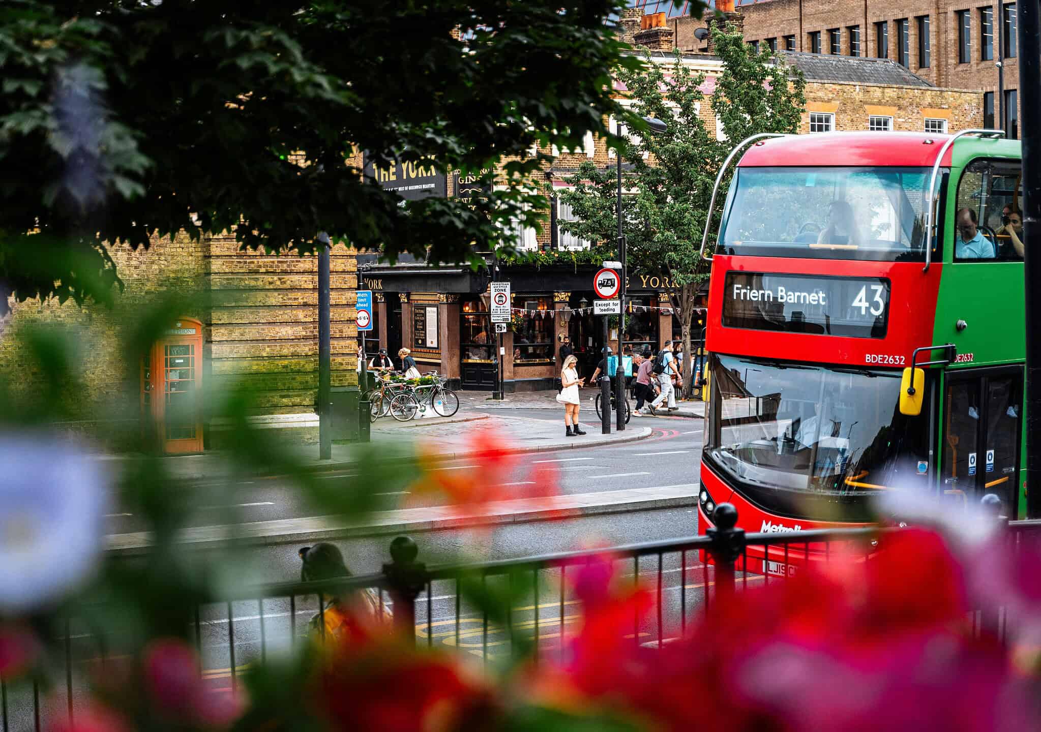View of North London streets with a red and green double-decker bus, pedestrians, and office buildings, showcasing the vibrant business district near Belcor London.