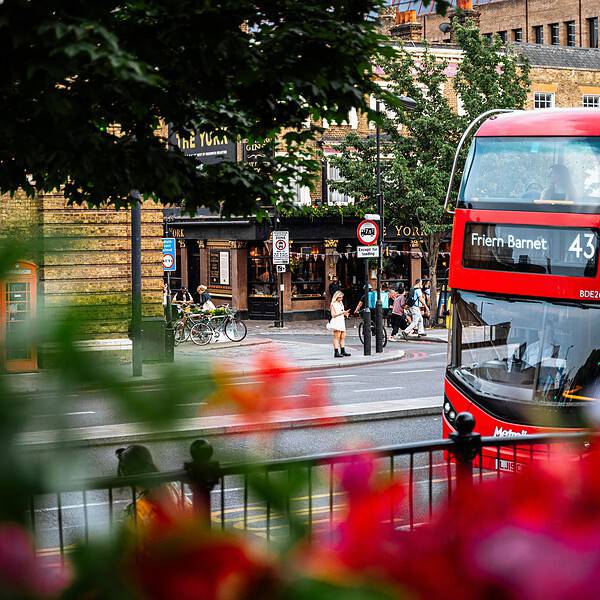 View of North London streets with a red and green double-decker bus, pedestrians, and office buildings, showcasing the vibrant business district near Belcor London.