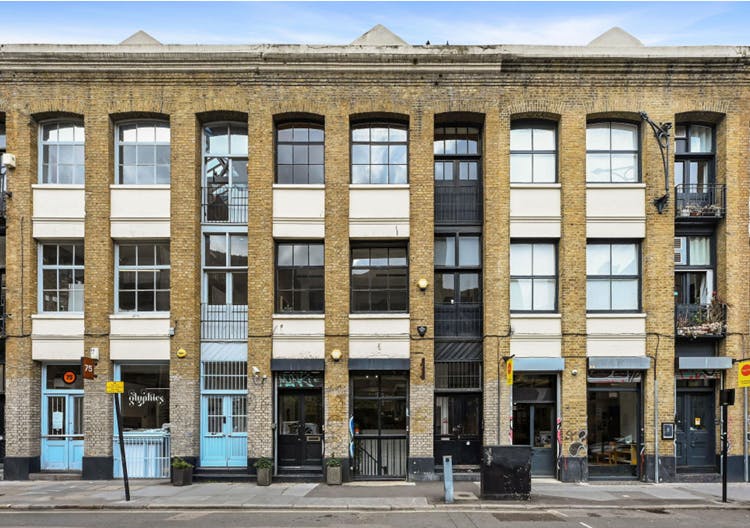 A modern brick building with large windows and retail shops on the ground floor, located on a city street in London, showcasing urban architecture and commercial spaces.