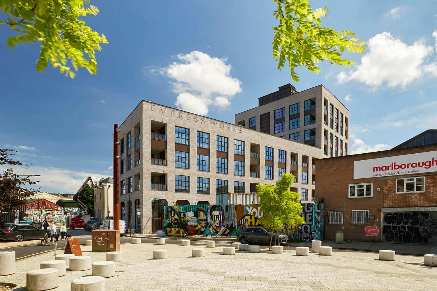 BELCOR building in London with modern architecture, graffiti art on the walls, and a vibrant urban plaza under a bright blue sky with scattered clouds.