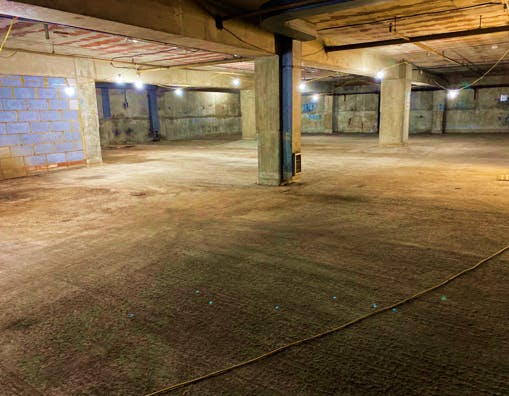 A spacious, unfinished underground parking garage with concrete pillars and walls, illuminated by overhead lighting, ready for construction or renovation.