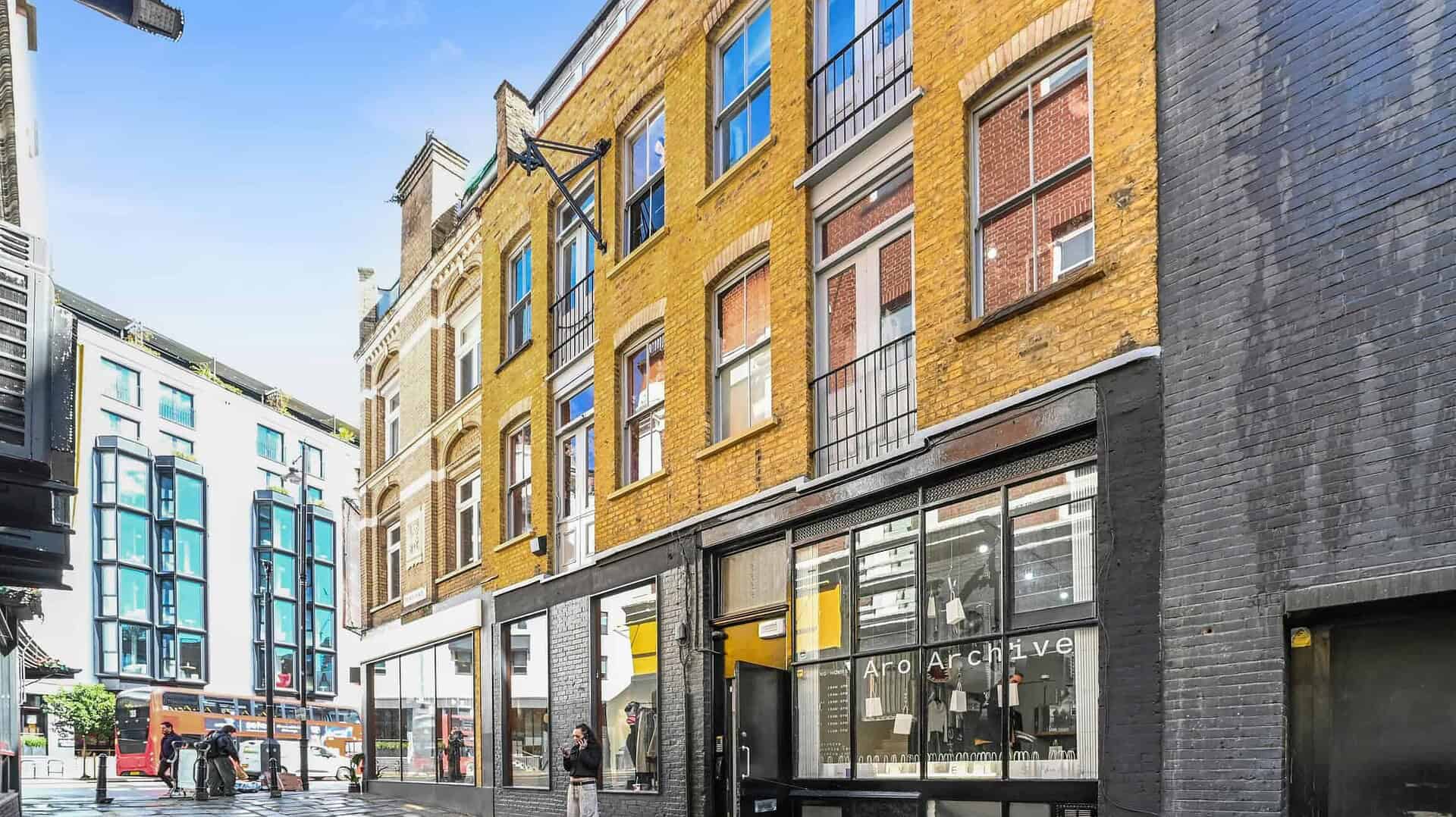 Modern storefront of BELCOR in London, featuring large glass windows and a black facade, situated on a cobblestone street with surrounding contemporary and historic buildings.