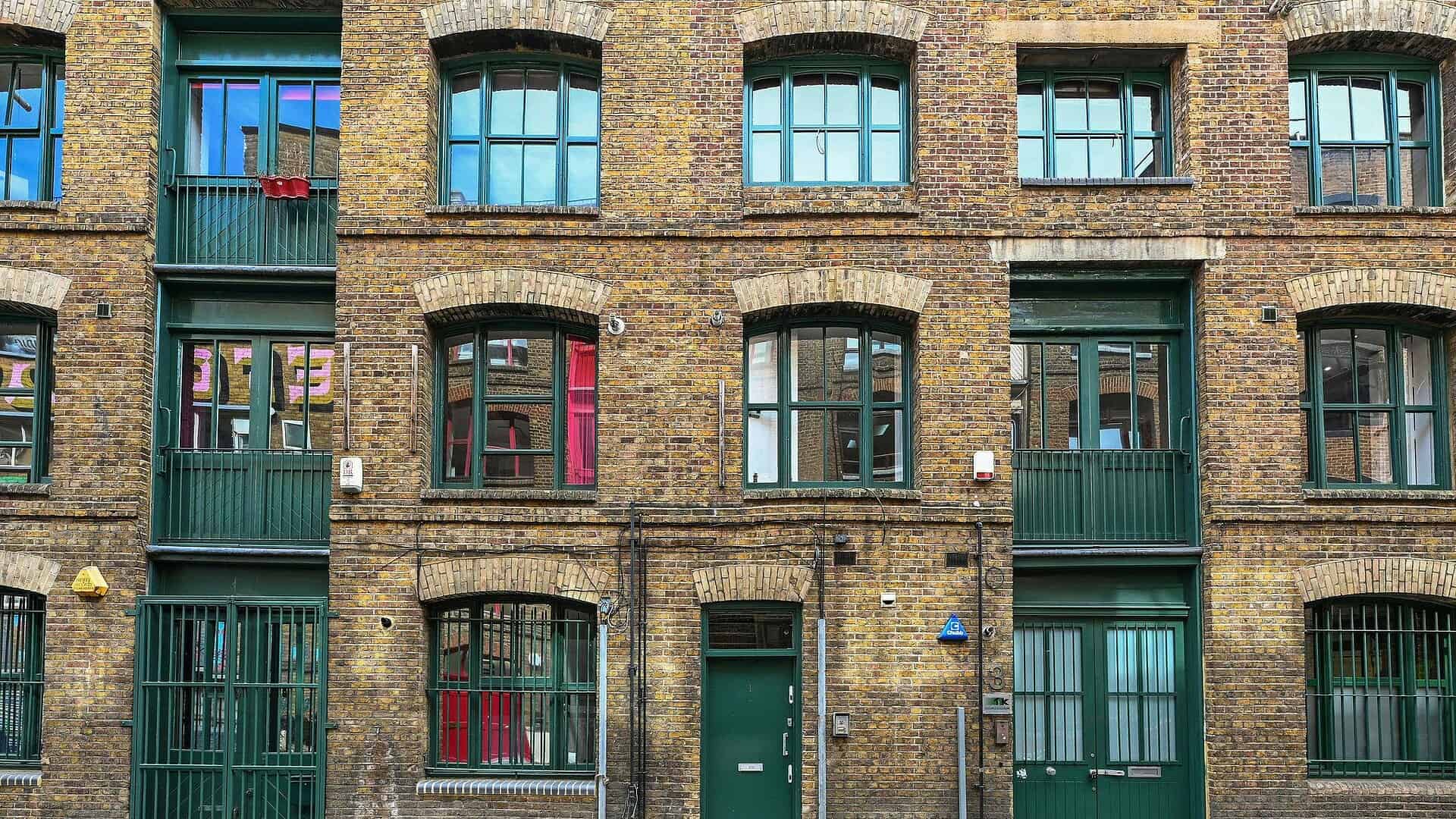 A vibrant brick building with colorful window frames and green balconies, showcasing urban architecture and residential design in London.