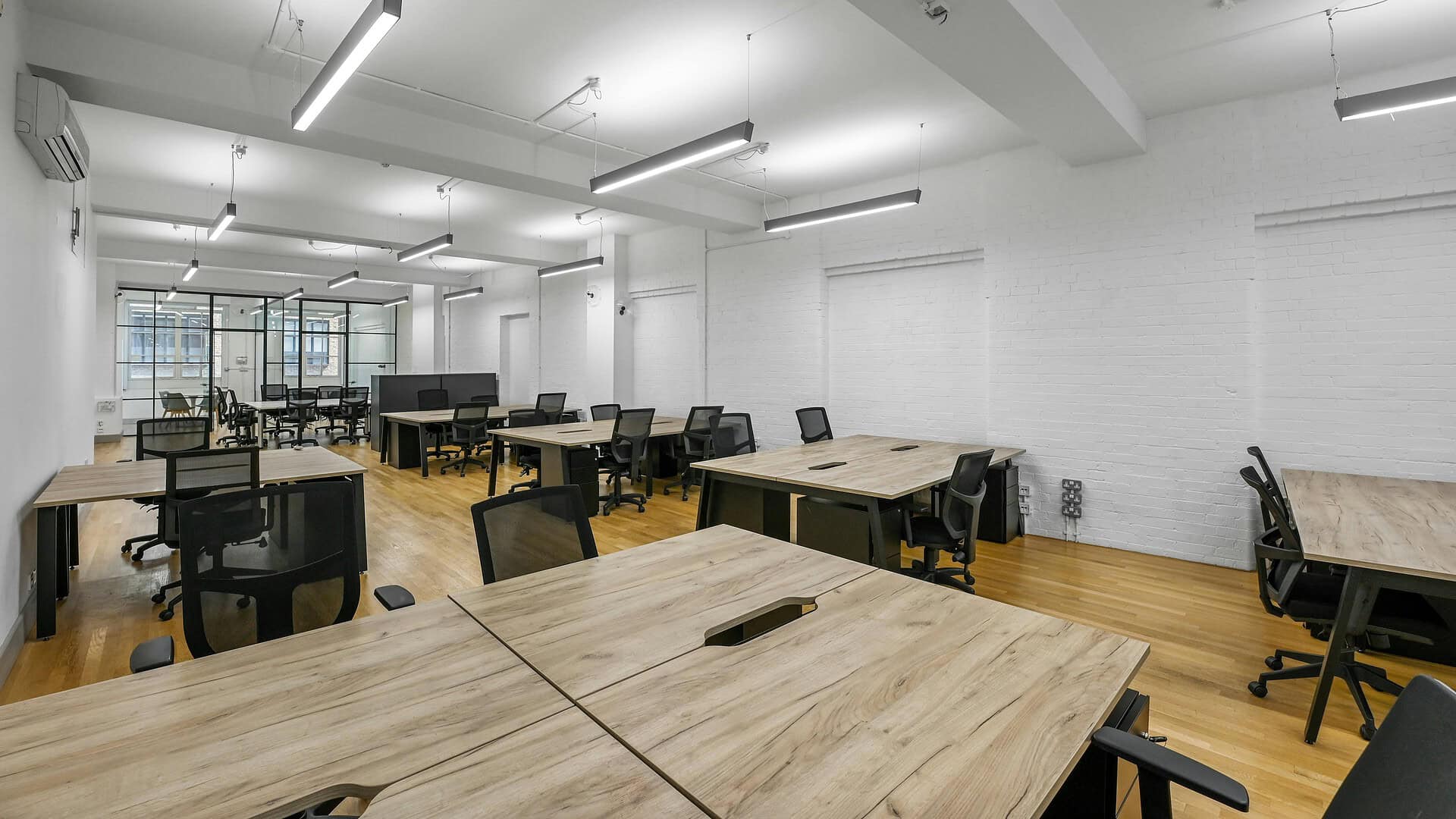 Modern open-plan office space with wooden desks, ergonomic chairs, and bright lighting, ideal for collaborative work and professional business environments.