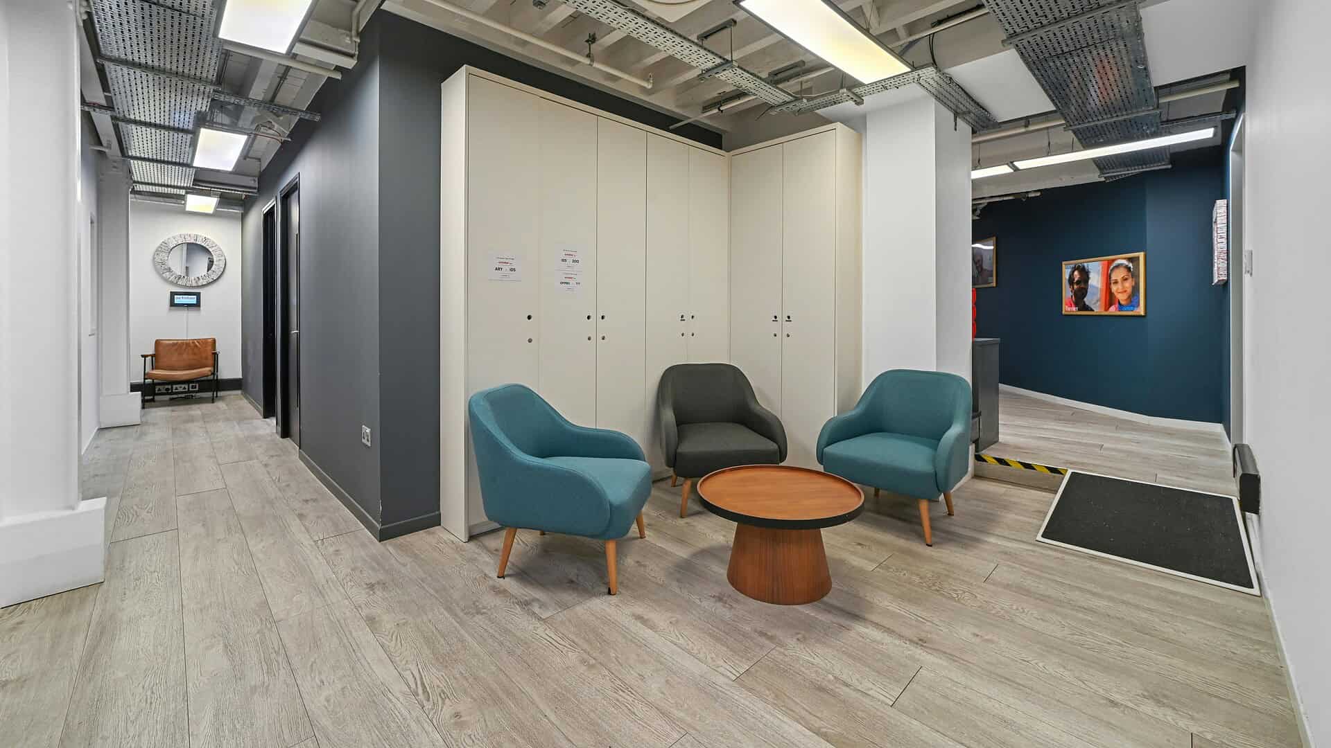 Modern office lounge at Benwell Studios with stylish blue and black chairs, wooden coffee table, and contemporary decor in a professional workspace environment.