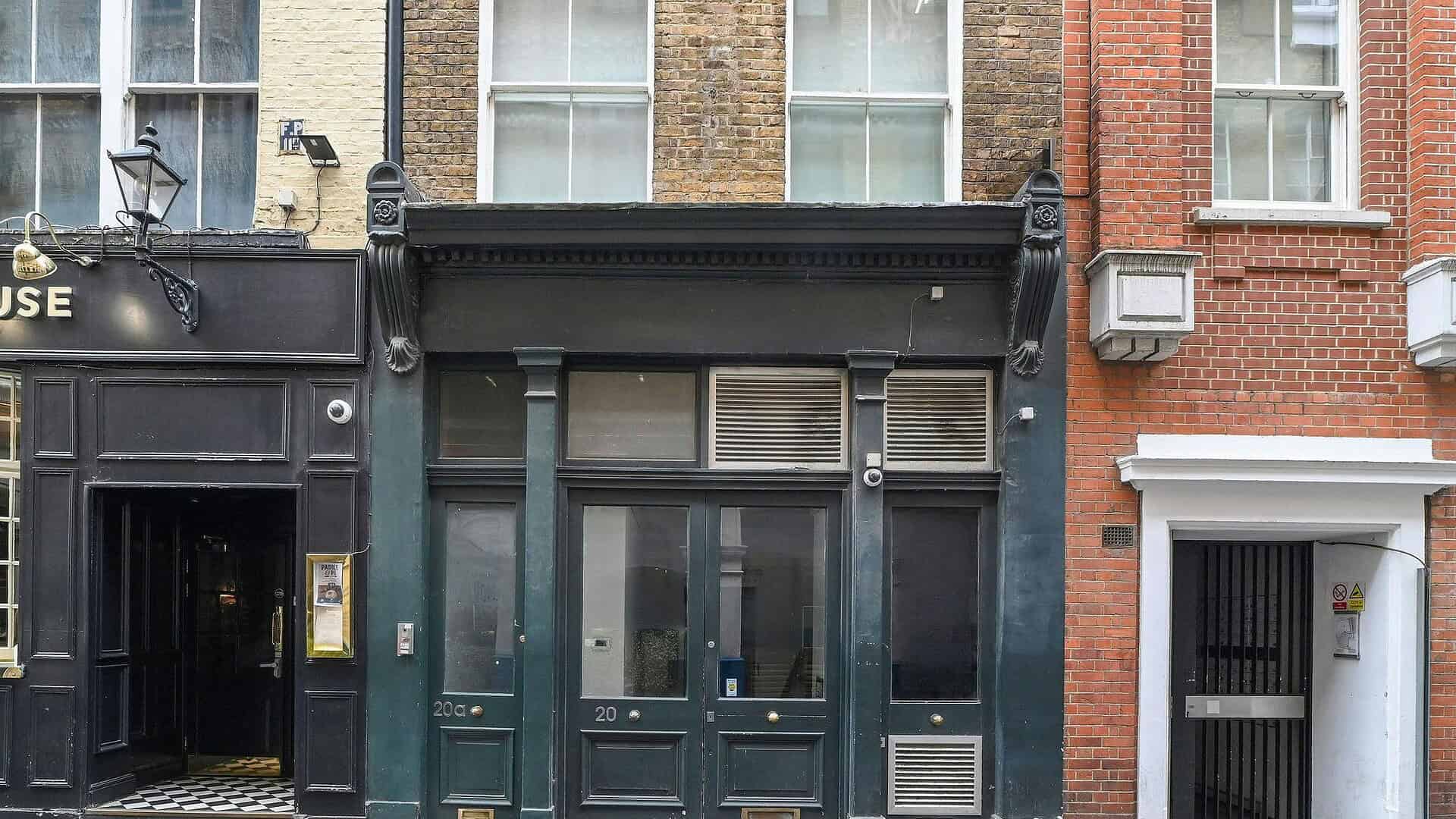 A storefront of BELCOR located at 20 Artillery Lane, featuring dark green doors and windows, with surrounding brick buildings in London, UK.