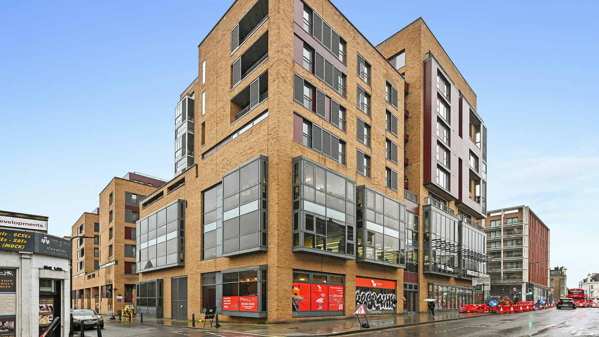 A contemporary commercial and residential building at 14 Dalston Lane, E8 3AZ, showcasing modern design with large glass storefronts and mixed-use spaces in a vibrant London neighborhood.