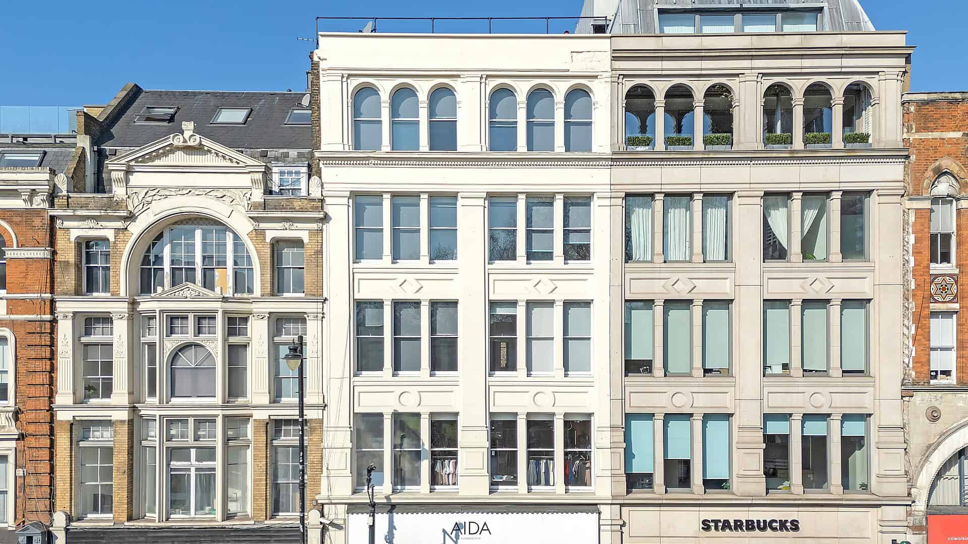 A row of contemporary buildings with retail shops on the ground floor, including Starbucks and MIDA, showcasing urban architecture and vibrant city life.