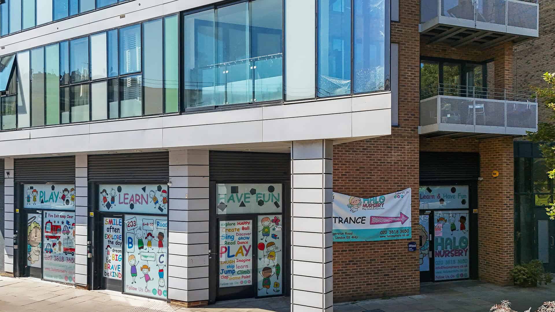 Modern commercial units with colorful children's play and learning signs at 203 Haggerston Road E8 4HU, London, featuring large glass windows and brick facade.