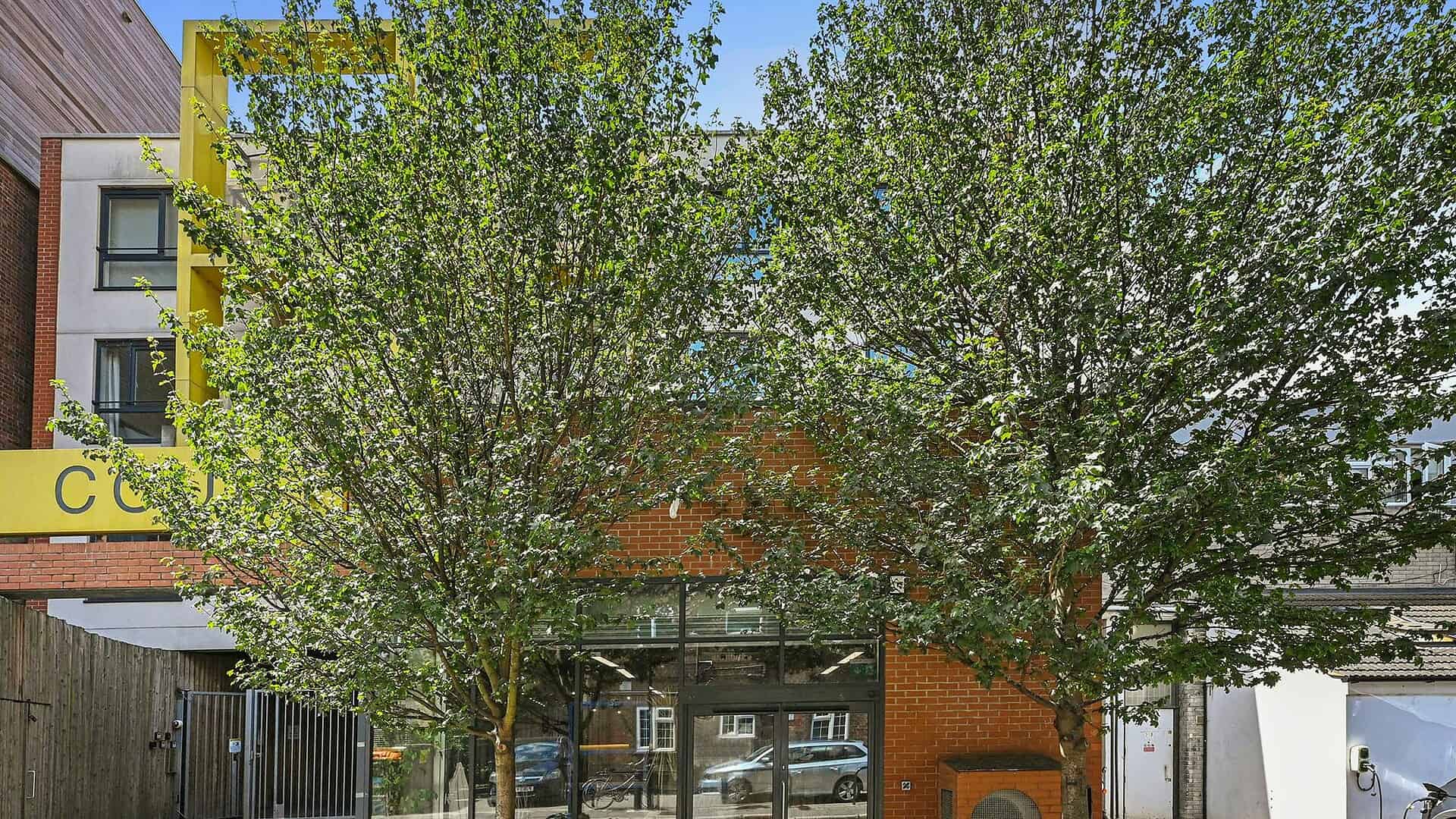 Contemporary commercial building with large glass windows, surrounded by lush green trees, located at 1a Dunn Street E8 2DG, London.