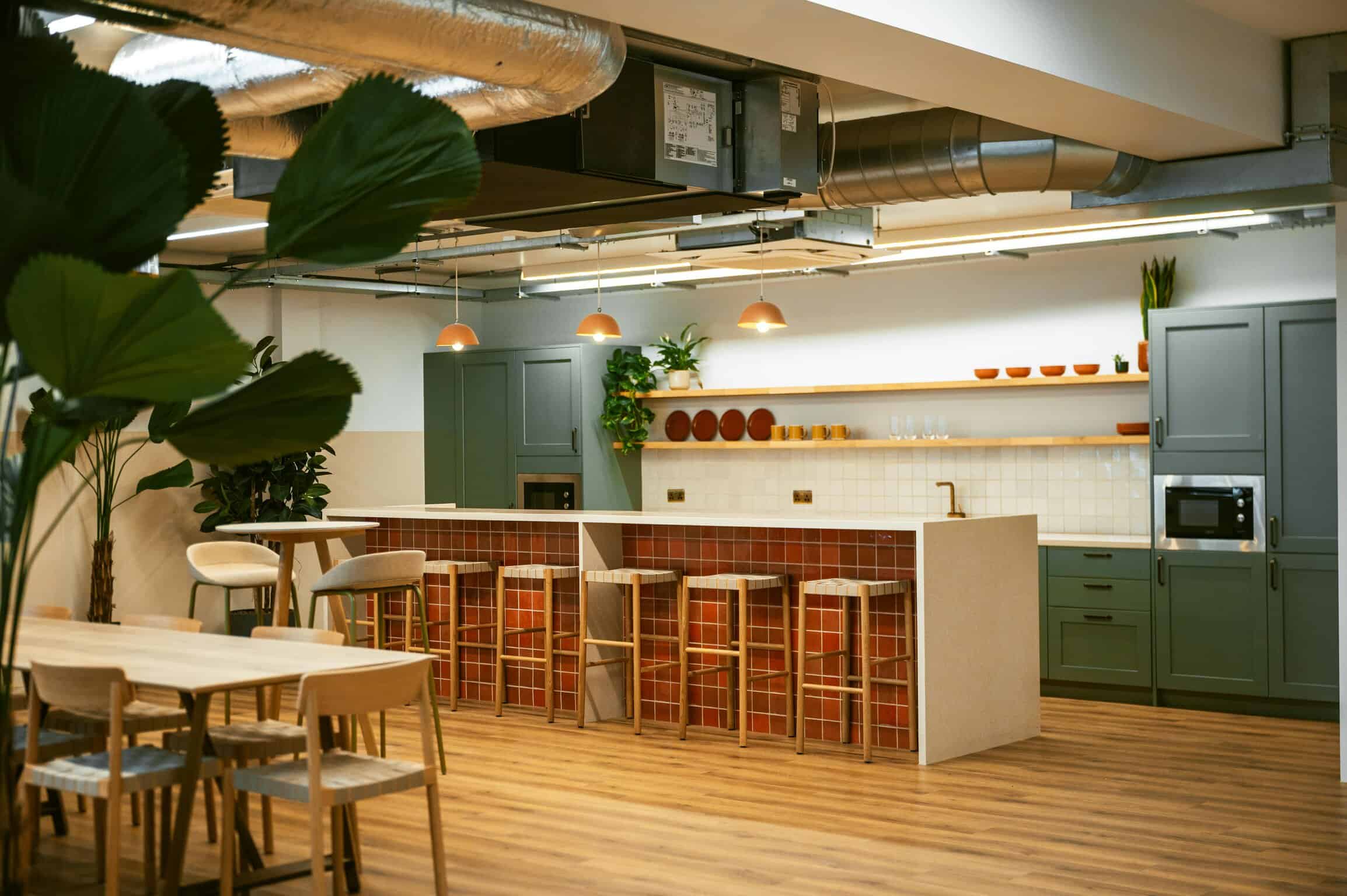 Modern interior kitchen with green cabinets, terracotta tiles, wooden bar stools, and minimalist decor in a stylish space.