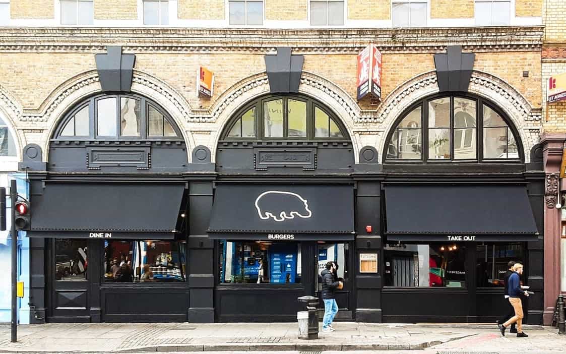 Modern burger restaurant storefront with black exterior, neon pig logo, and arched windows, specializing in dine-in, takeout, and gourmet burgers in London.