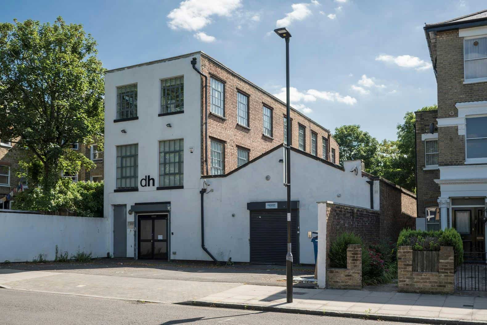 A modern white and brick commercial building with large windows, situated on a street with trees and a clear blue sky, representing contemporary architecture and urban development.