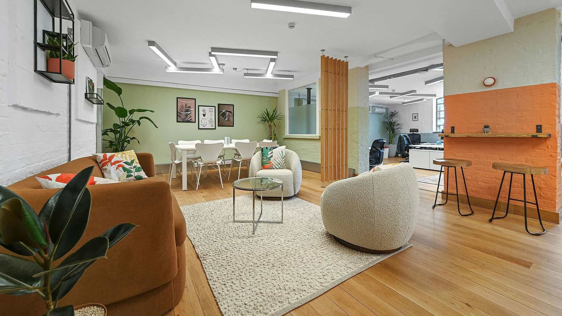Bright and welcoming office lounge with contemporary furniture, green accent wall, and natural light, perfect for collaborative work and relaxation at 11-29 Fashion Street Unit 1.4 E1 6PX.