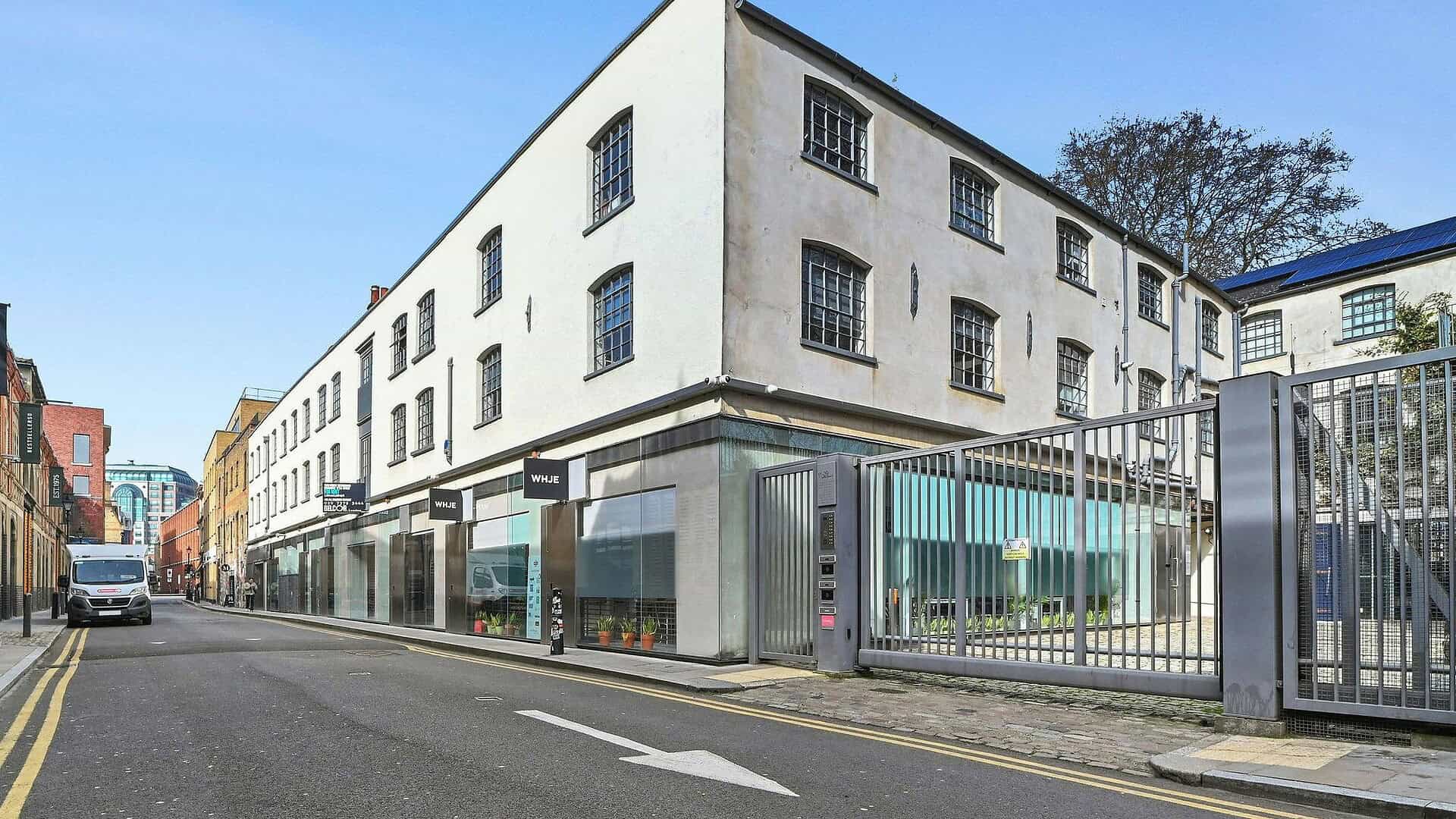 A modern commercial building with large glass windows and a gated entrance, located on a city street in London, featuring contemporary architecture and retail spaces.