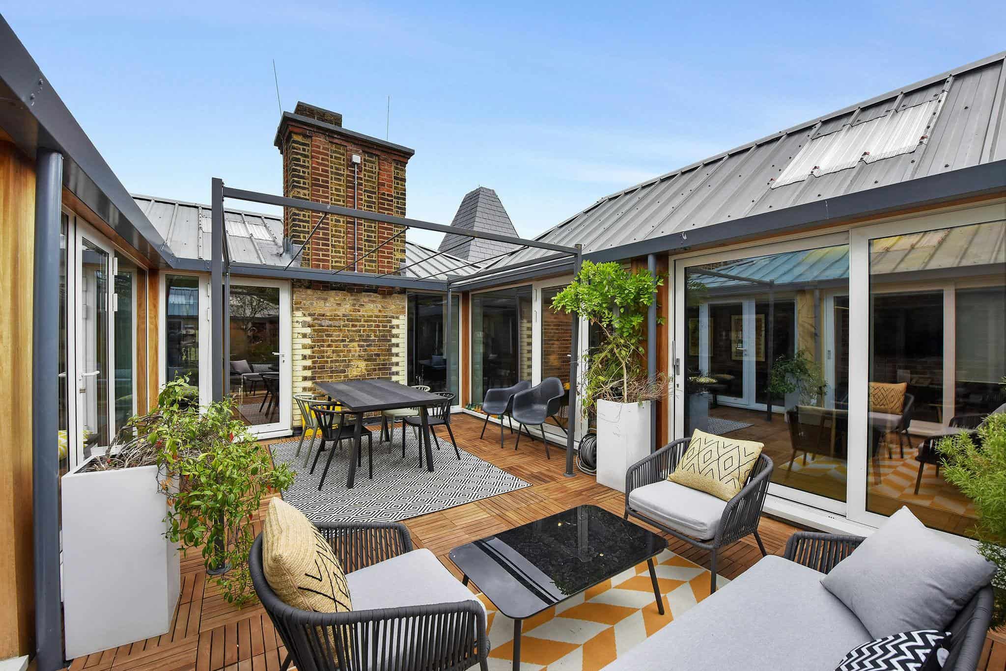 A rooftop terrace with modern outdoor furniture, potted plants, and glass doors leading to indoor spaces, offering a stylish and comfortable urban outdoor area in London.