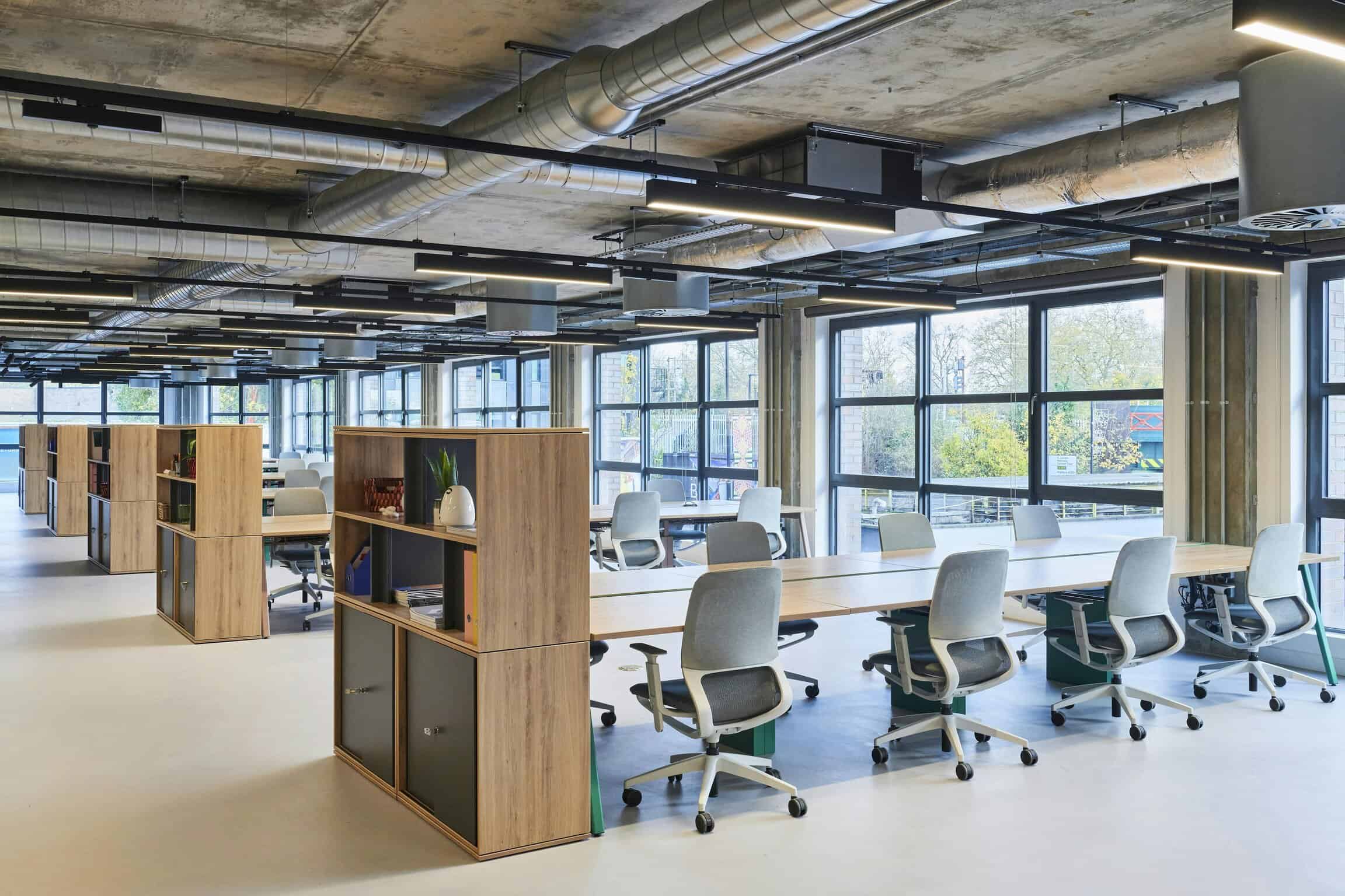 Modern office workspace with large windows, ergonomic chairs, and wooden storage units, promoting productivity and a bright, open environment for collaborative work.