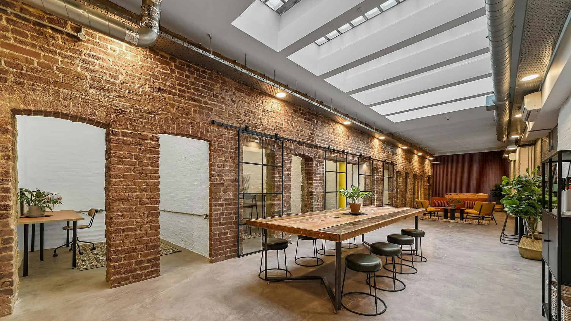 Bright and spacious coworking area featuring exposed brick walls, large windows, and a skylight, ideal for collaborative work environments and creative teams.