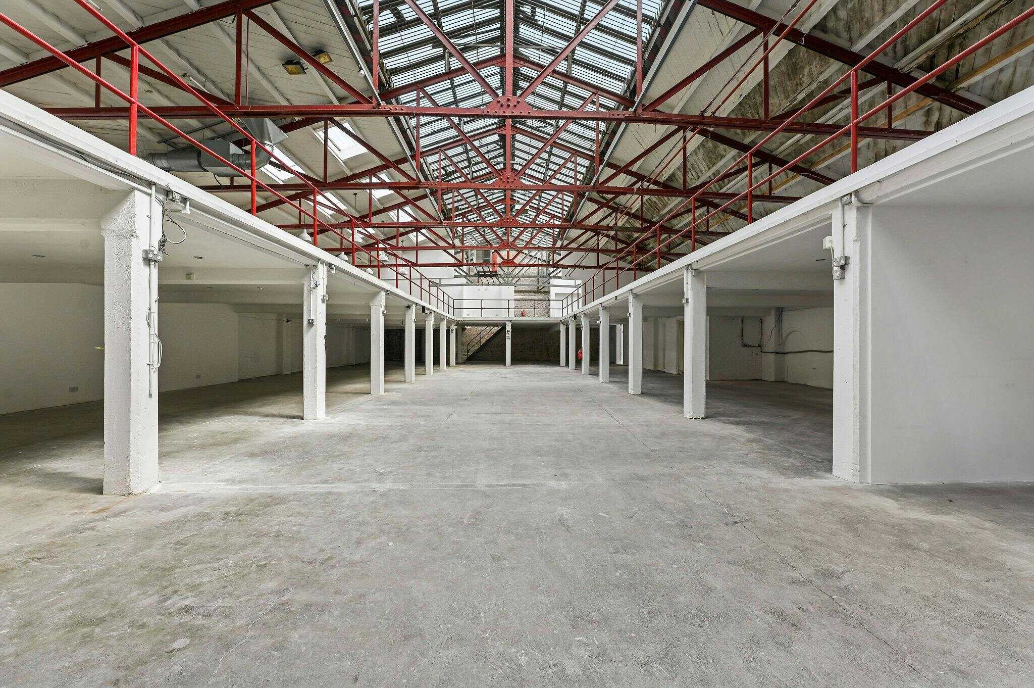 A spacious, empty industrial warehouse with high ceilings, exposed red steel beams, and large skylights providing natural light, ideal for storage or commercial use.